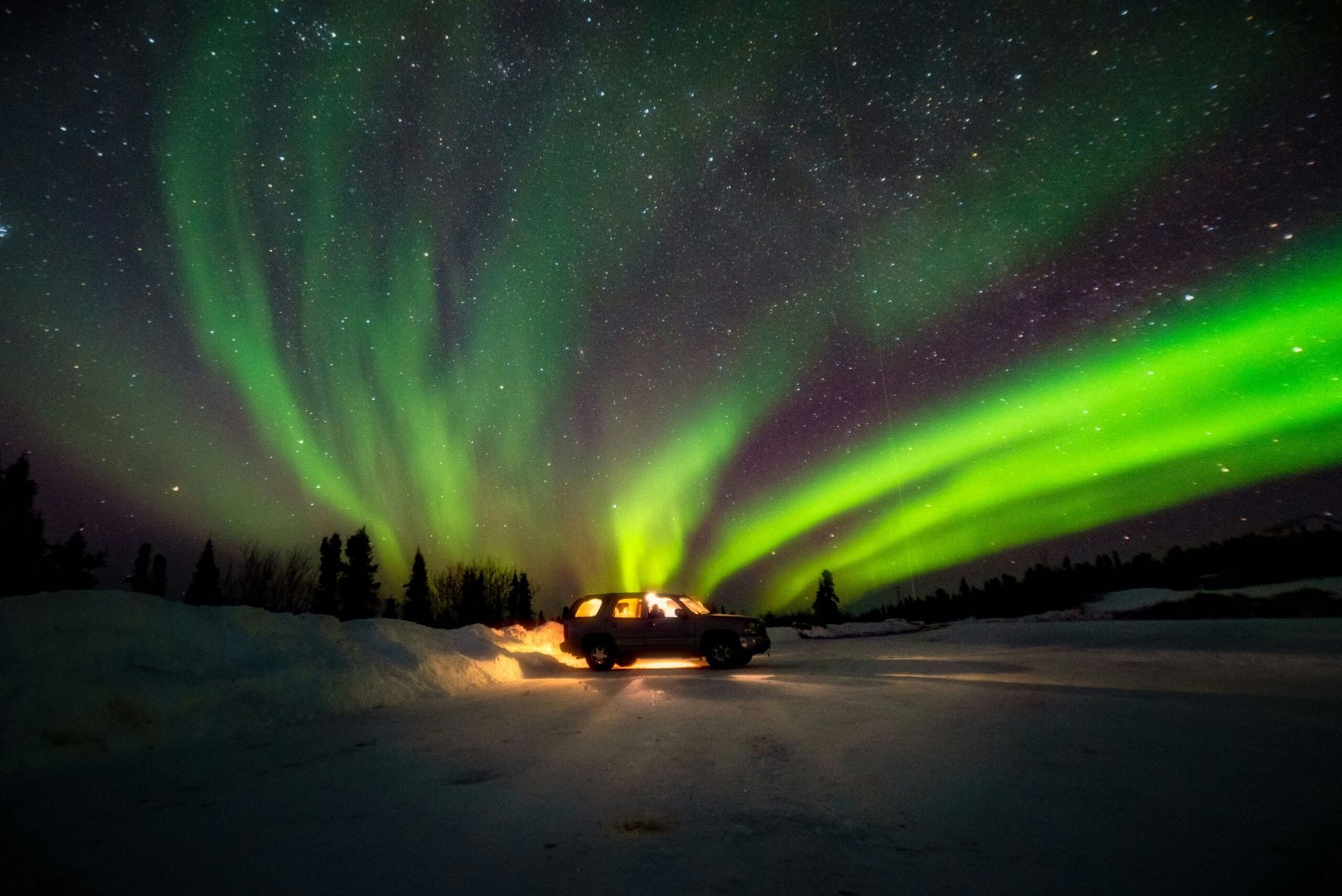 Truck driving on a snowy Alaska road under green and purple northern lights